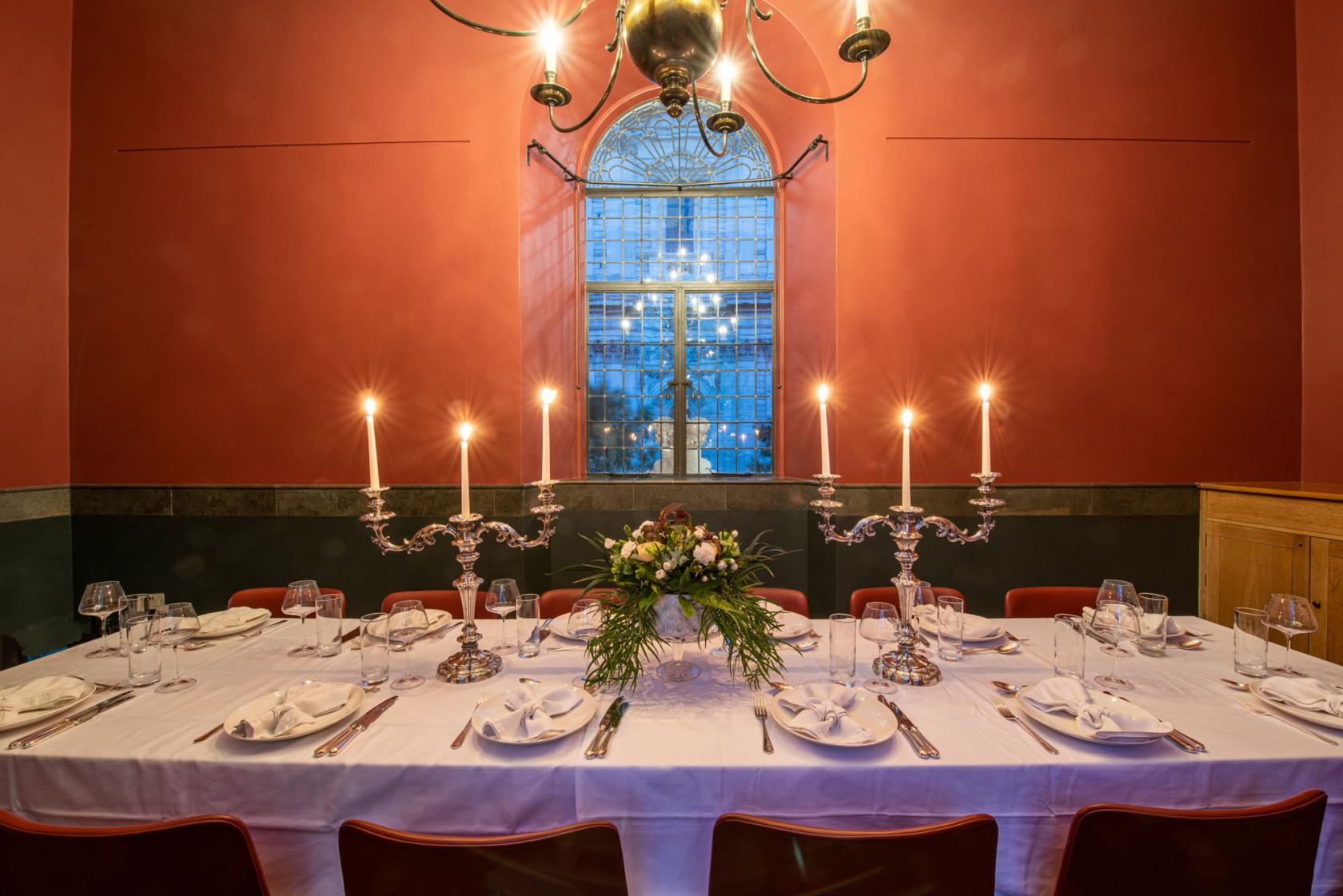 A bar with a long table set for dining, white linens, candelabras, and a large arched window at Temple Bar London.