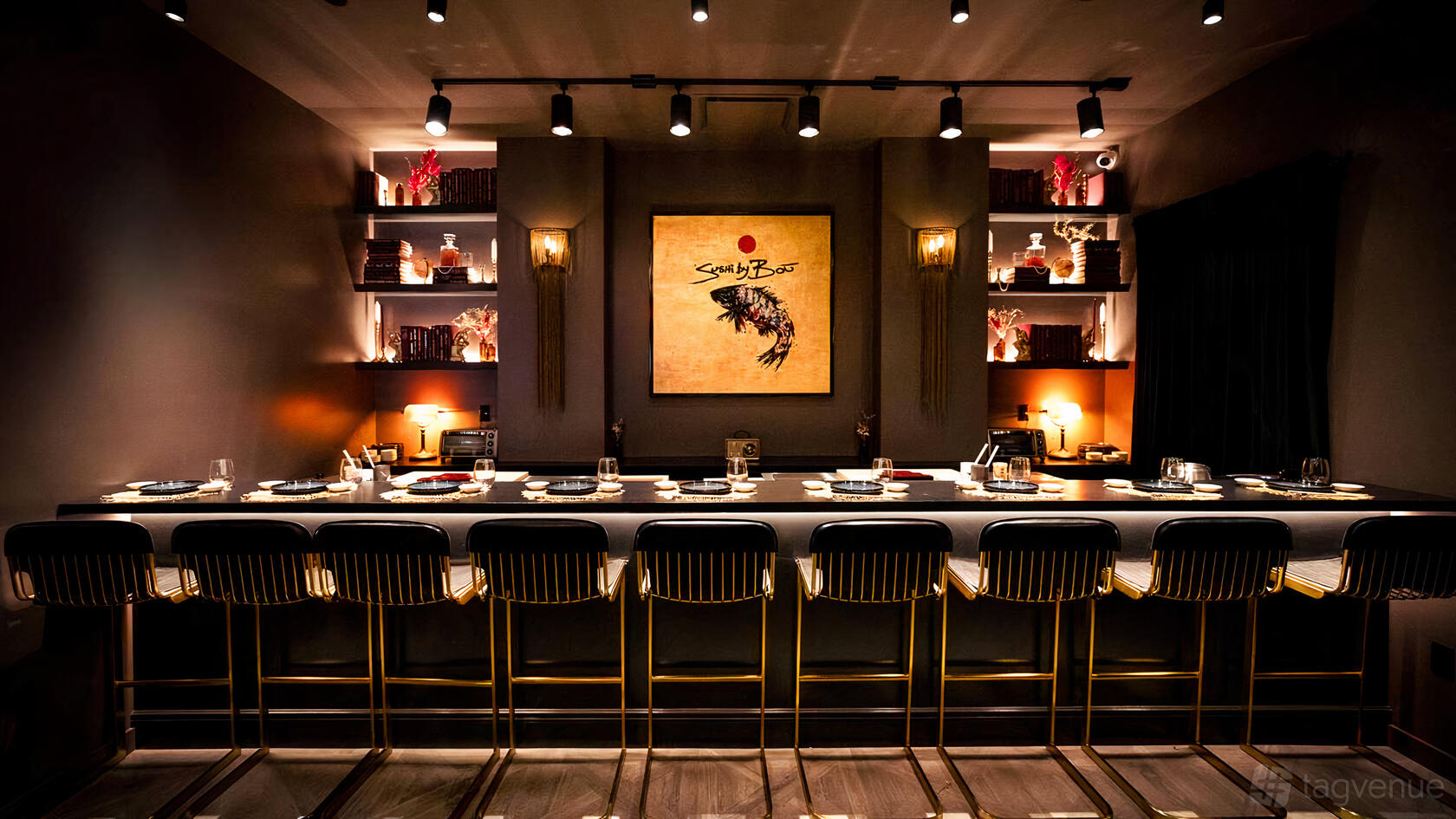 A restaurant with a sushi bar, gold barstools, ambient spotlighting, and decorative shelves at Sushi by Bou Chelsea.