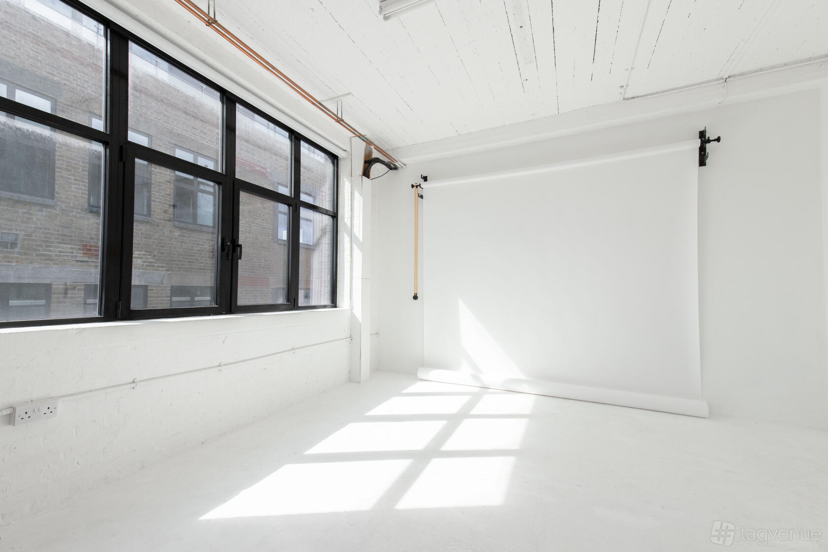 A photo studio with white walls, a large window, and a floor-to-ceiling white backdrop at Soif Studios.