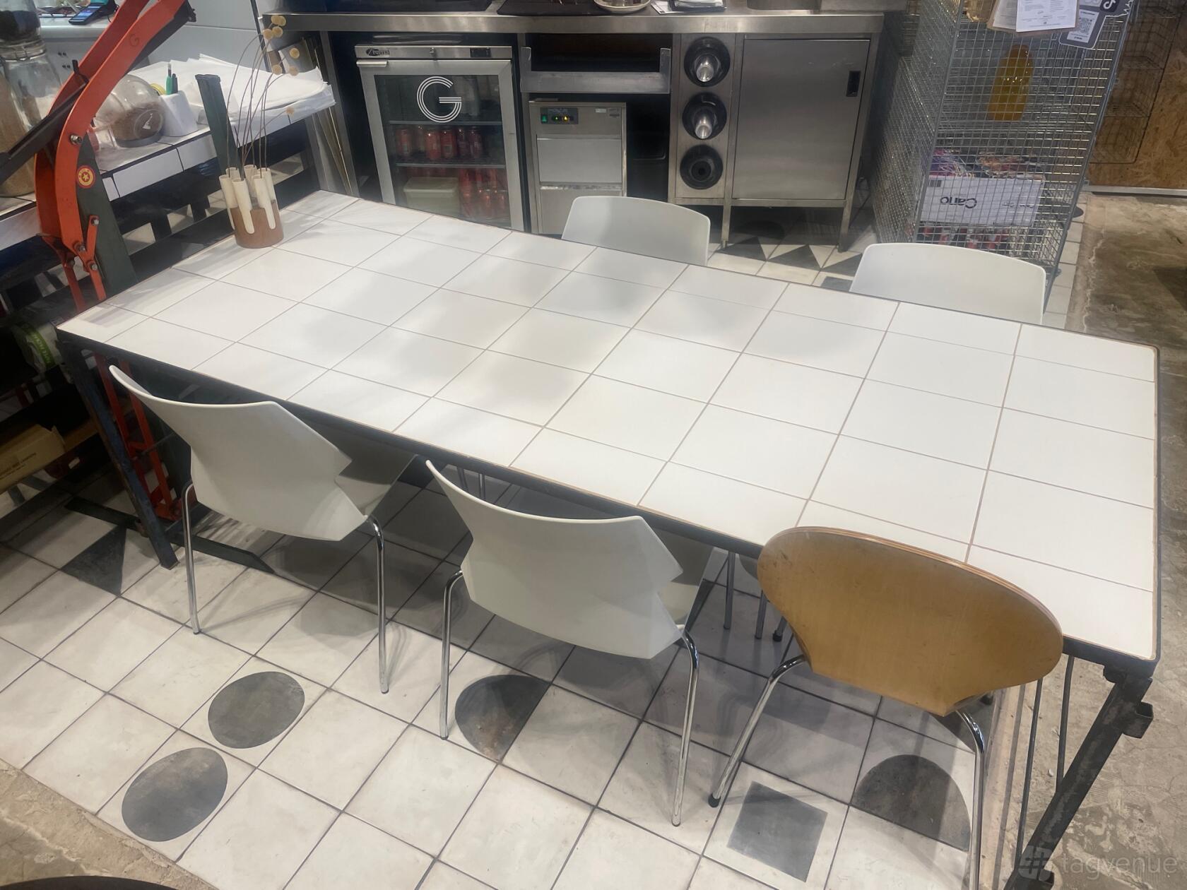 A restaurant table for eight with white tile surface and mixed white chairs at G Asian Canteen.