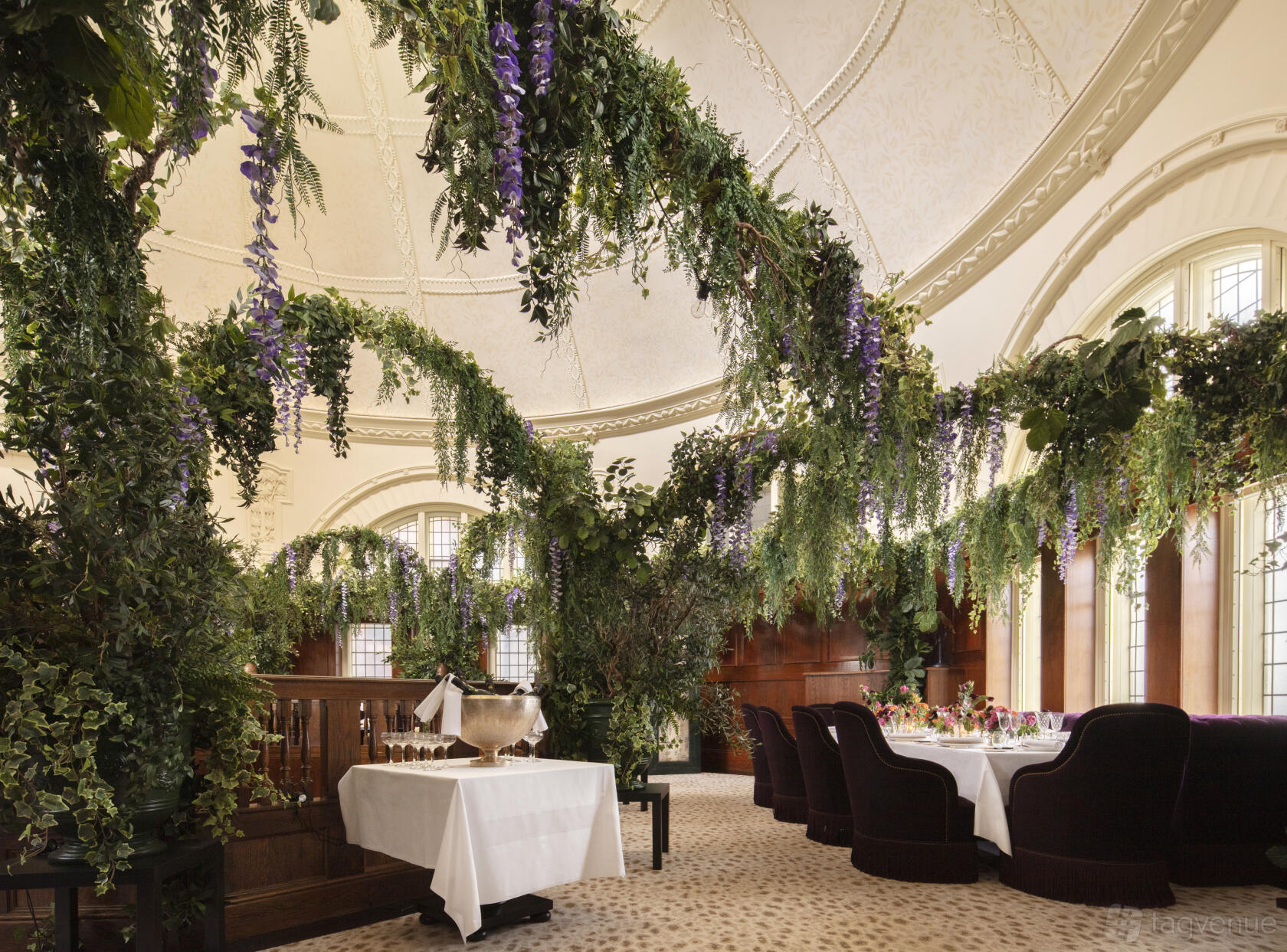 An event space with arched windows, ornate dome ceiling, and hanging greenery at L'oscar London