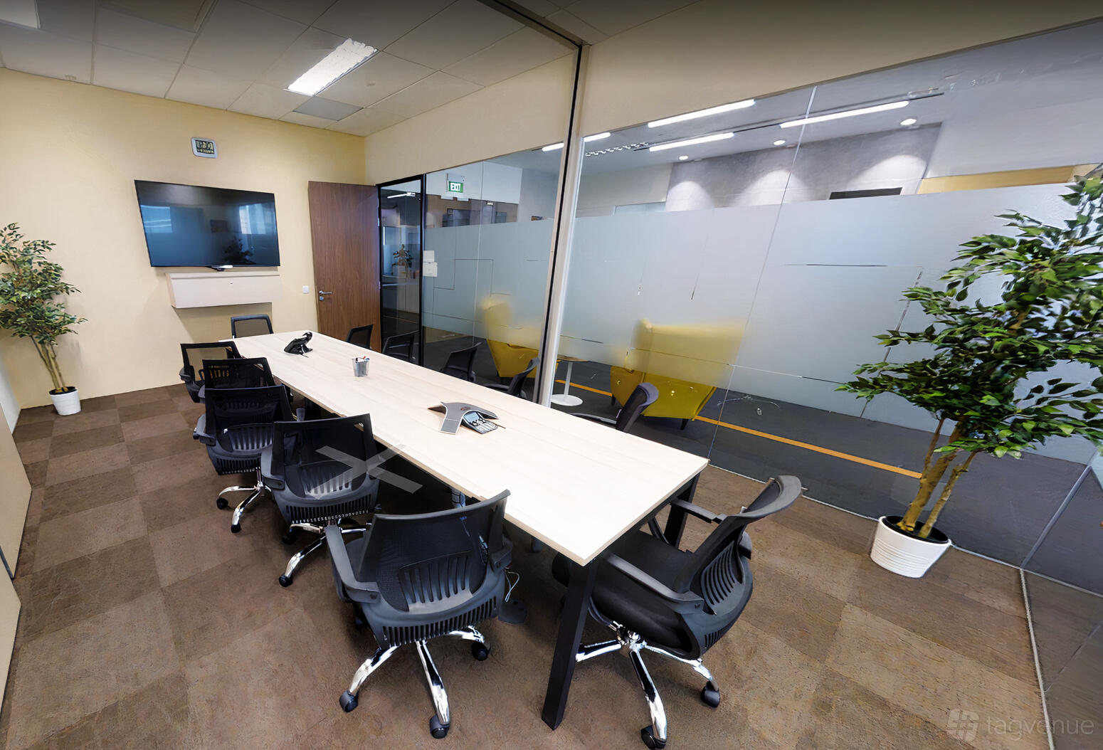 A boardroom with a long meeting table, black office chairs, glass walls, and potted plants at Tokio Marine Centre.