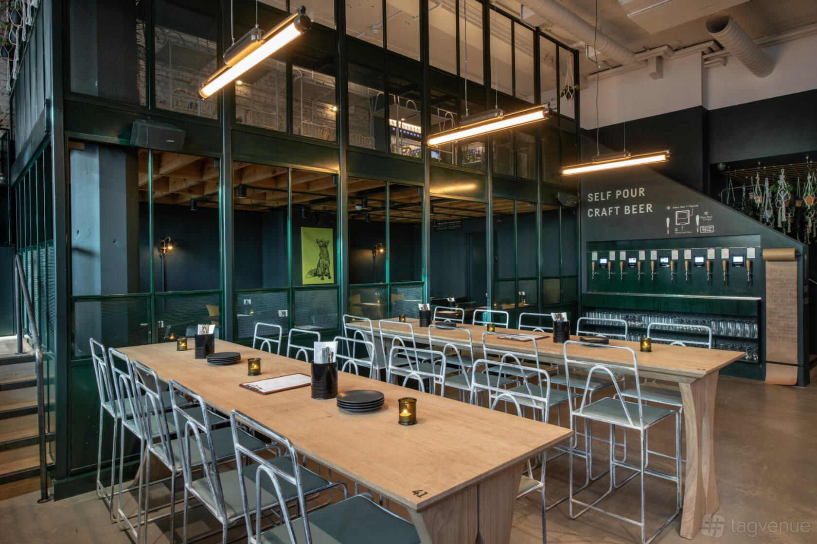 A bar with long wooden tables, metal chairs, and a self-pour craft beer wall at Vagabond Monument.