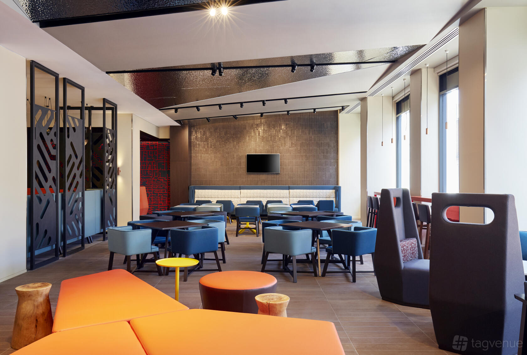 An event space in a hotel with floor-to-ceiling windows, colorful seating, and a wall-mounted TV at Holiday Inn Express Adelaide City Centre.