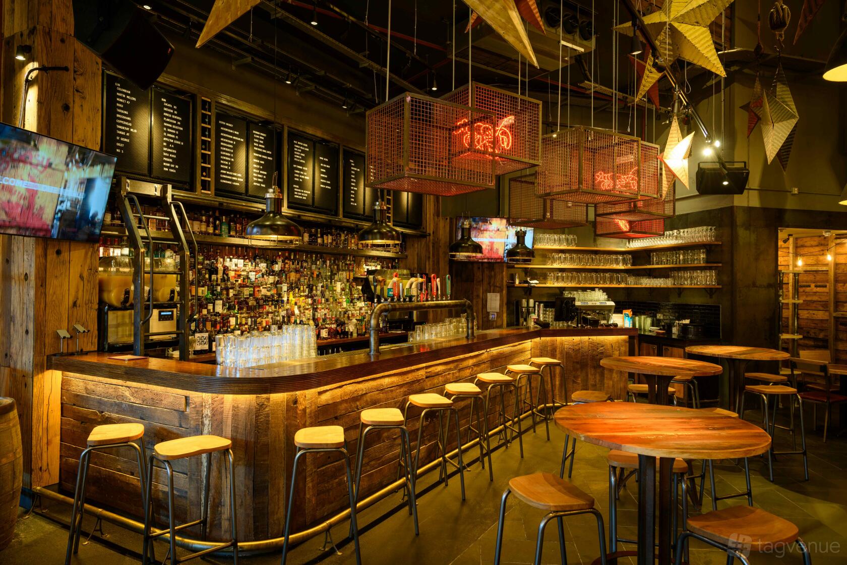 A restaurant with a wooden bar, high stools, round wooden tables, and overhead menu boards at BIG EASY - Bluewater.