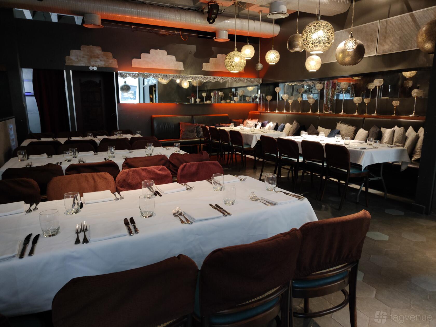 A function room with long tables covered in white linens, globe pendant lights, and mirrored walls at Cinnamon Kitchen.