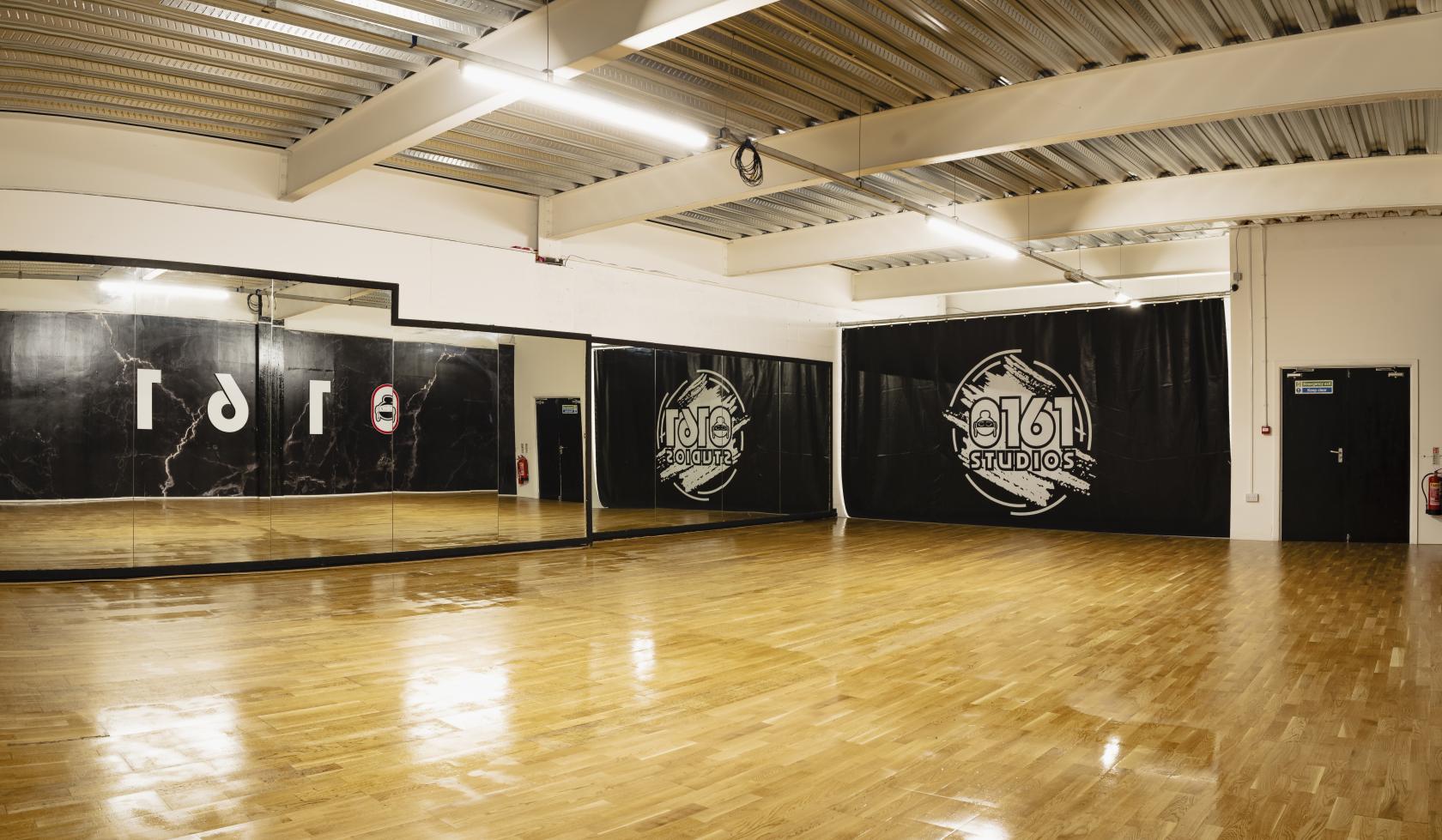 A dance studio with polished wooden floors, full-length wall mirrors, and exposed ceiling beams at 0161 Studios.