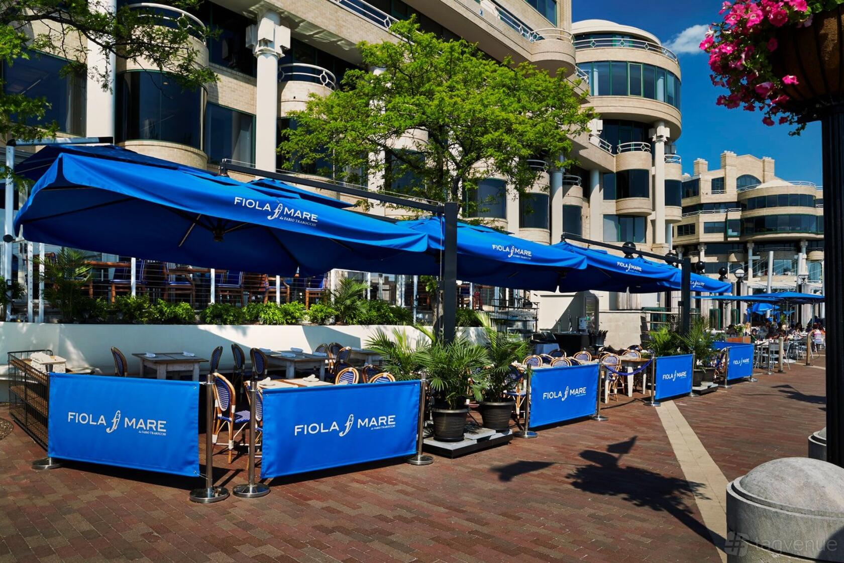 An outdoor restaurant patio with blue awnings, potted plants, and waterfront seating at Fiola Mare.