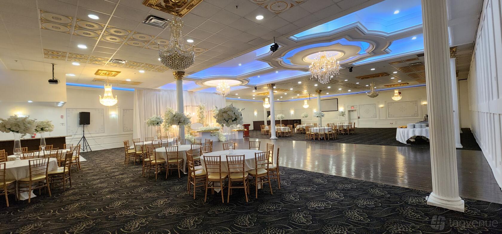 An event venue with crystal chandeliers, ornate ceiling details, round tables, and floral centerpieces at Royal King Event Centre.