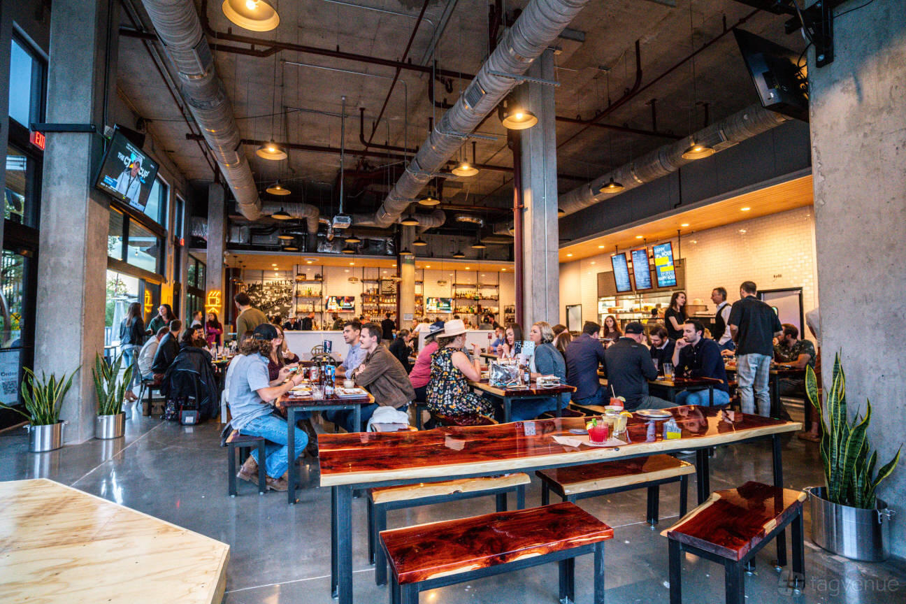 An event space in a restaurant with polished wood tables, exposed ductwork, and floor-to-ceiling windows at Industry.