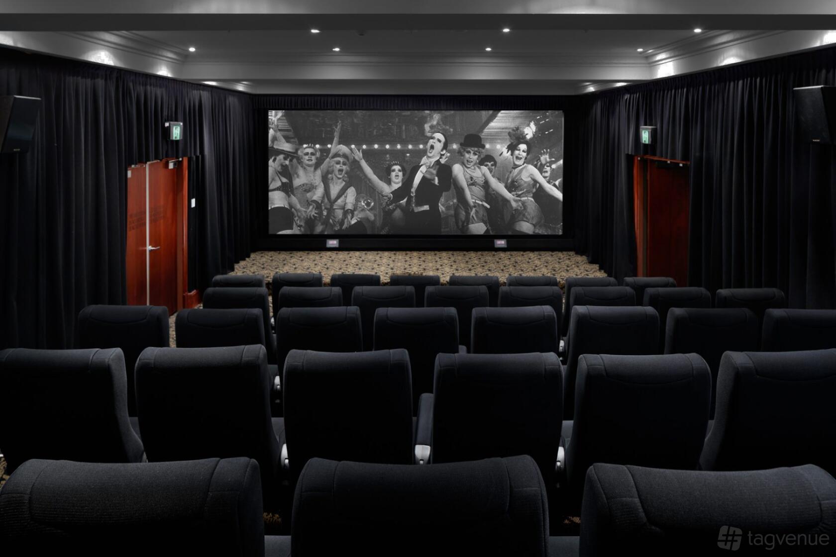 A screening room with tiered black seats, thick curtains, and a large projection screen at QT Sydney.