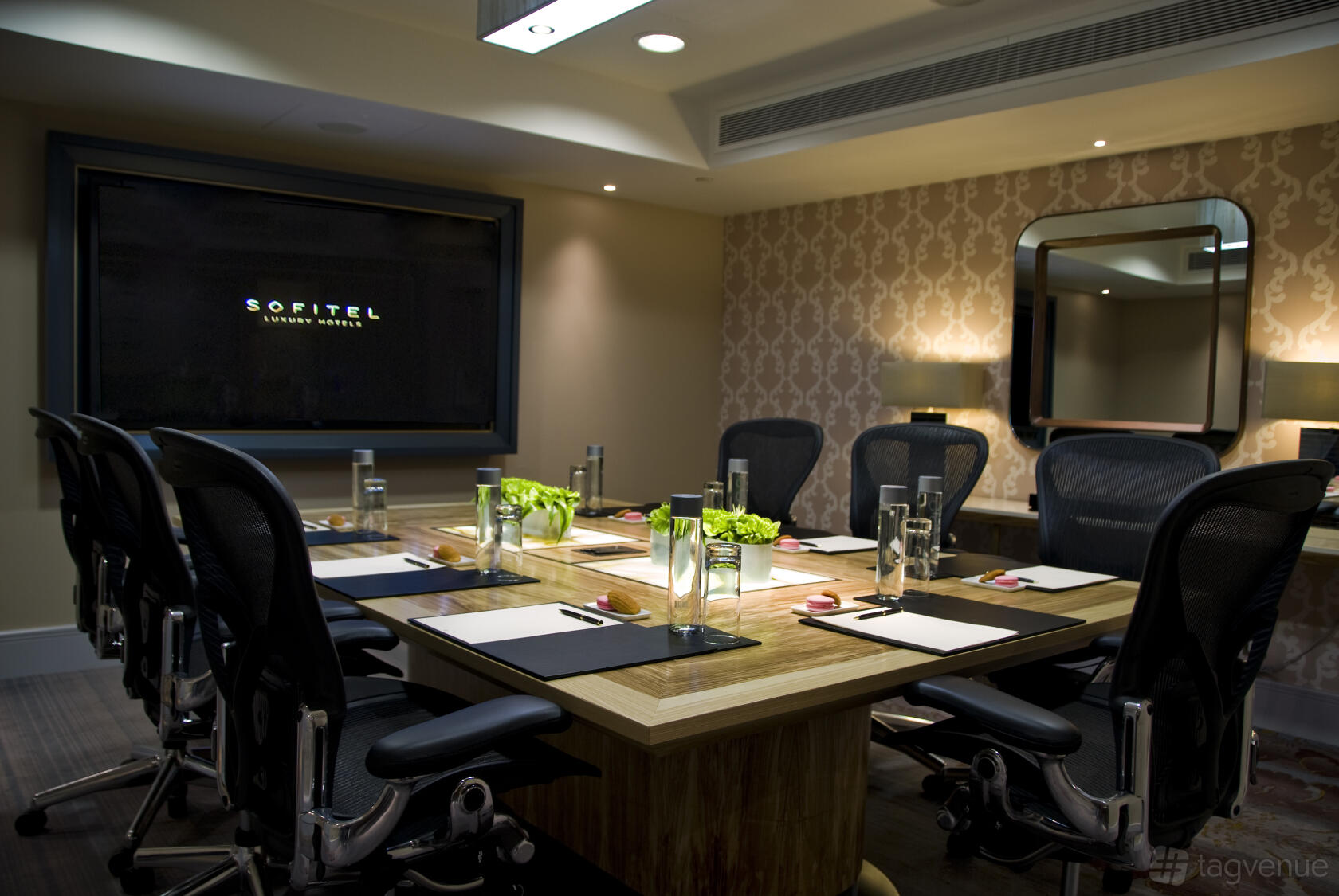 A meeting room with a wooden conference table, ergonomic chairs, notepads, and water glasses at Meetings & Events Venues.