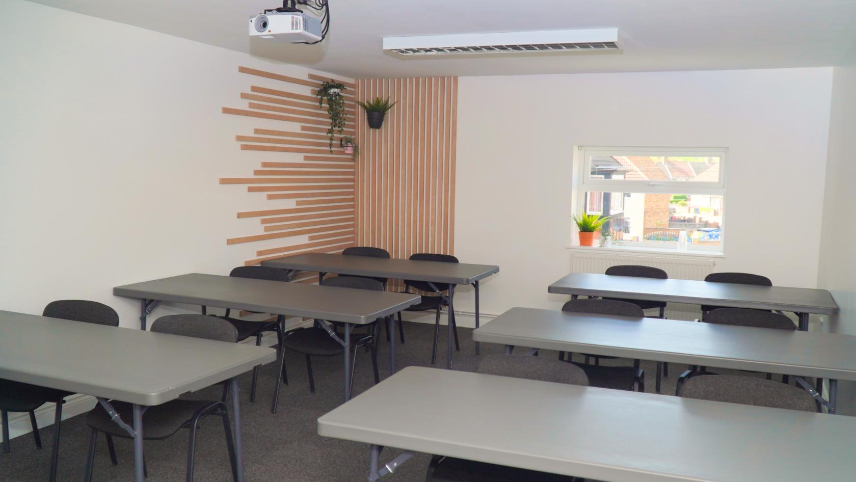 A meeting centre with rows of grey tables, black chairs, and a wall with wood slats and potted plants at Maggie O'Neill Business and Training Centre.