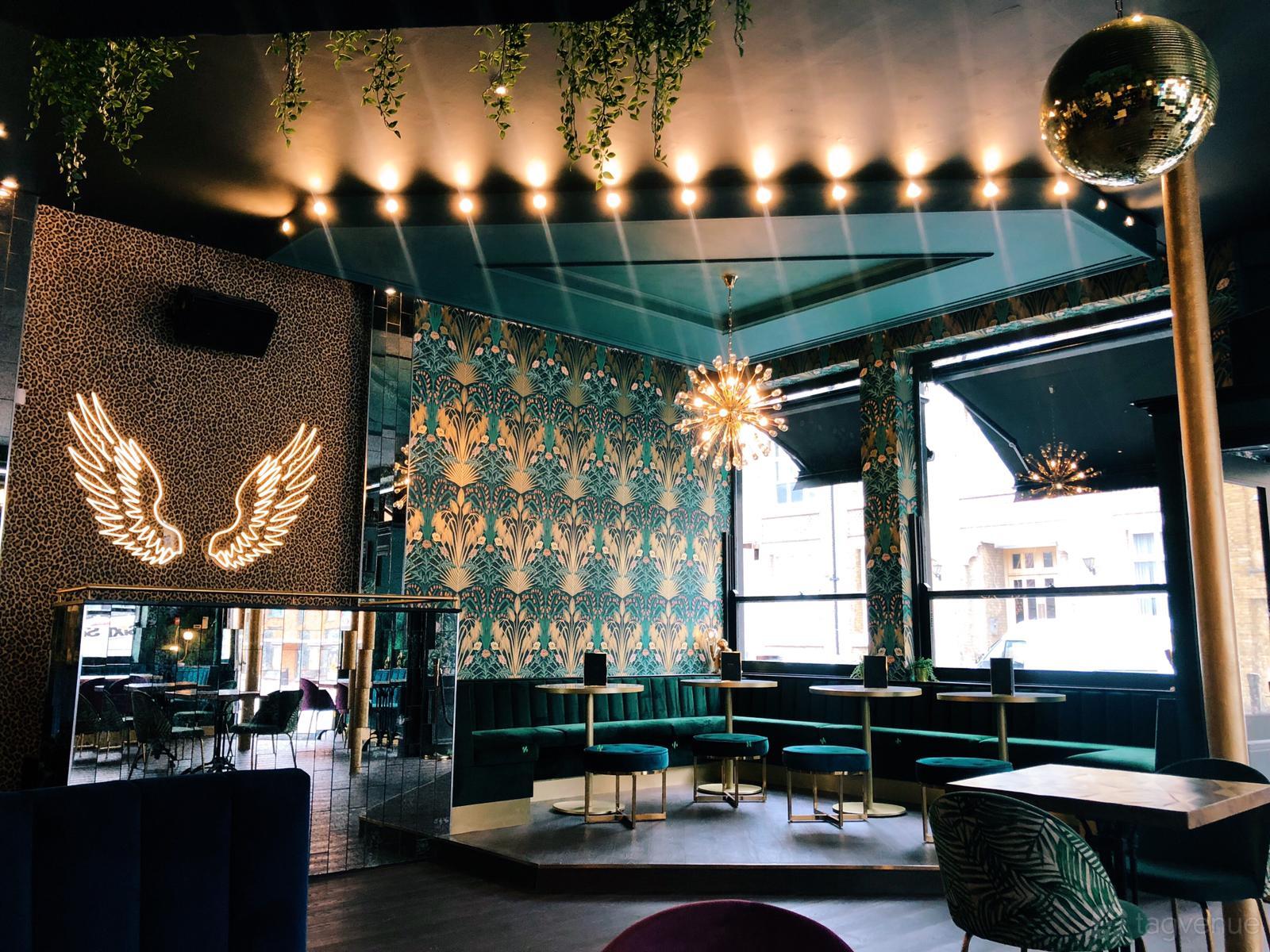 An event space in a cocktail bar with patterned wallpaper, booth seating, velvet stools, and a golden chandelier at Lost Society (Battersea SW11).