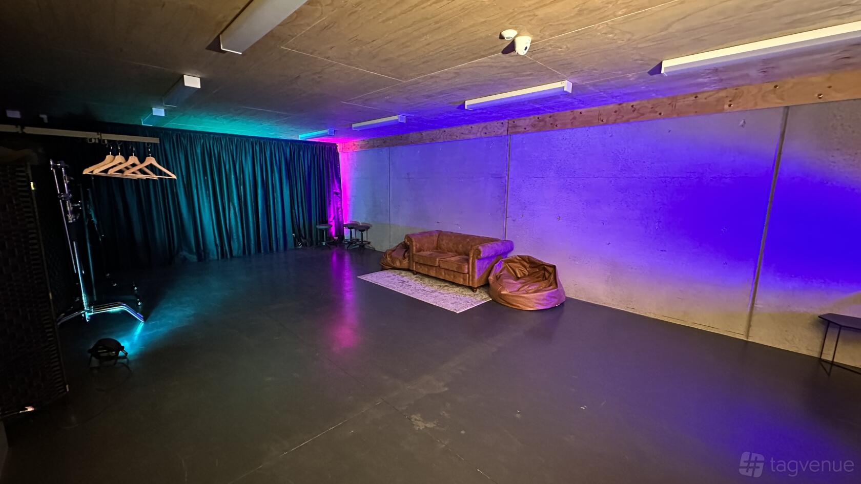 A recording studio with exposed concrete walls, wood ceiling, colored LED lighting, and a seating area at REKT Studios.