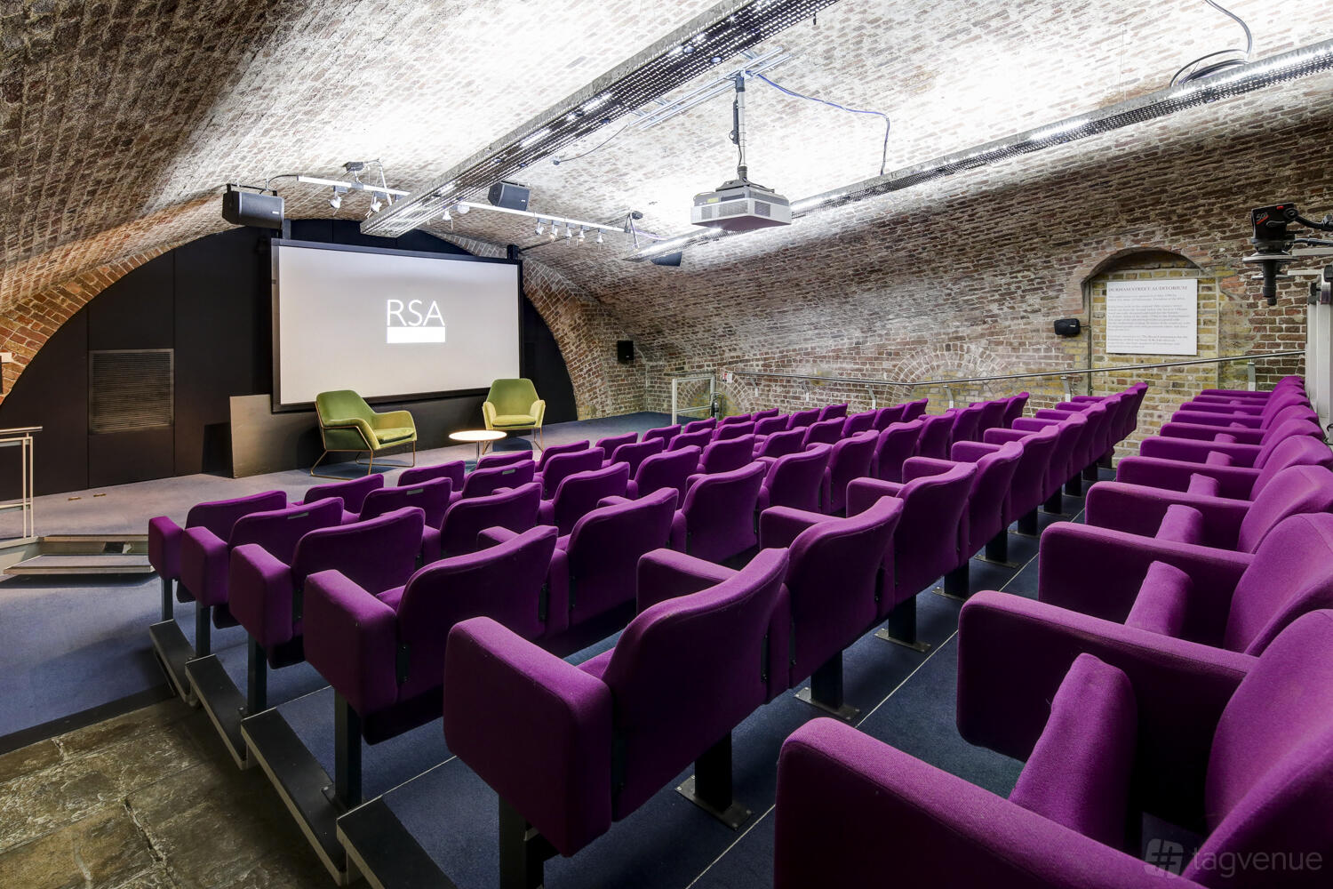An auditorium with purple theater seating, vaulted exposed brick ceiling, and projection screen at RSA House.