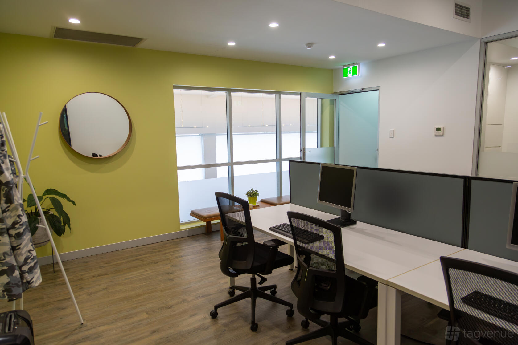 An office space with shared desks, computer monitors, rolling chairs, and a round wall mirror at Camperdown Quarters.