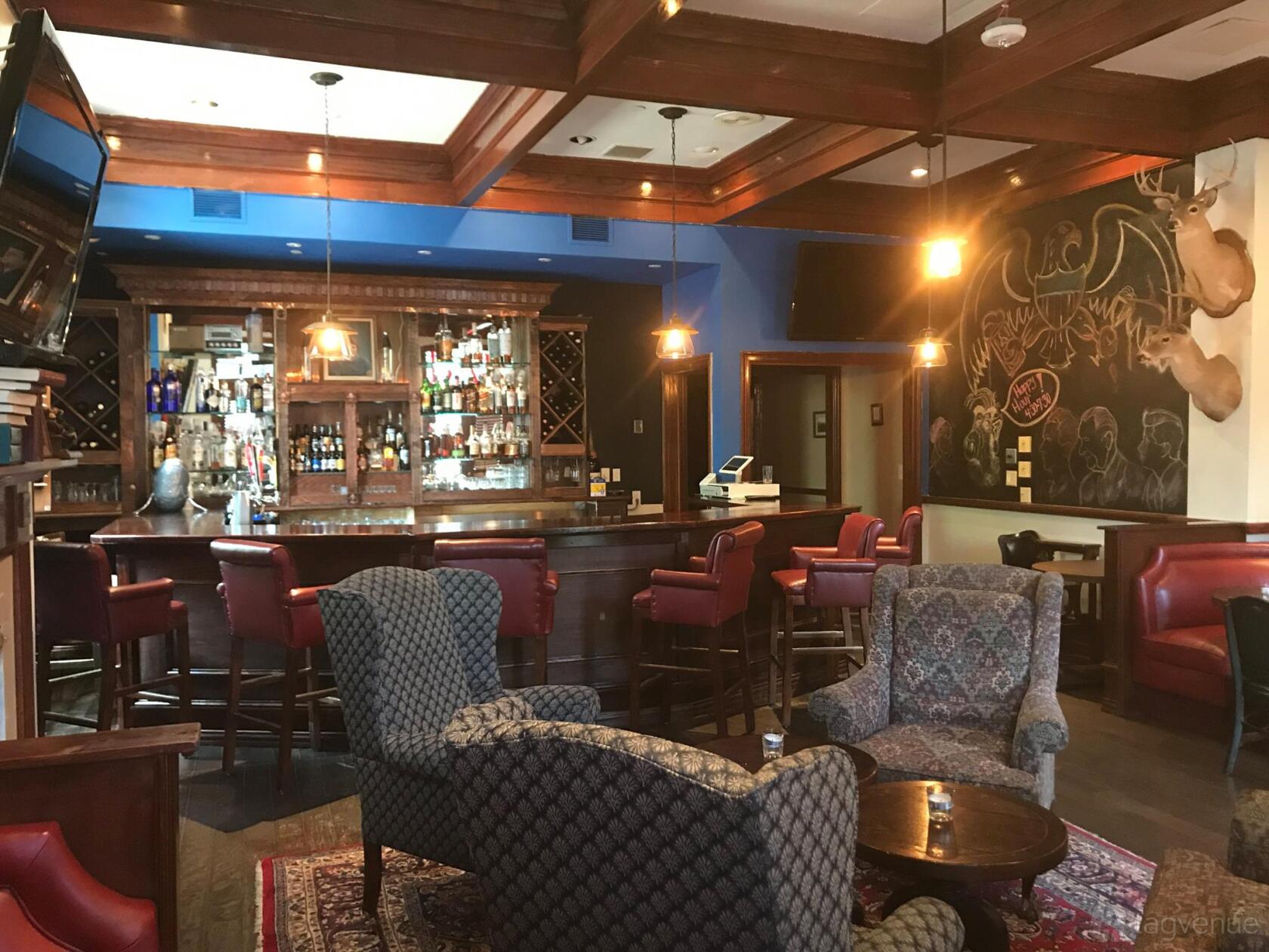 A bar with leather barstools, patterned armchairs, a wooden bar, and a chalkboard wall at Kennedy Room.