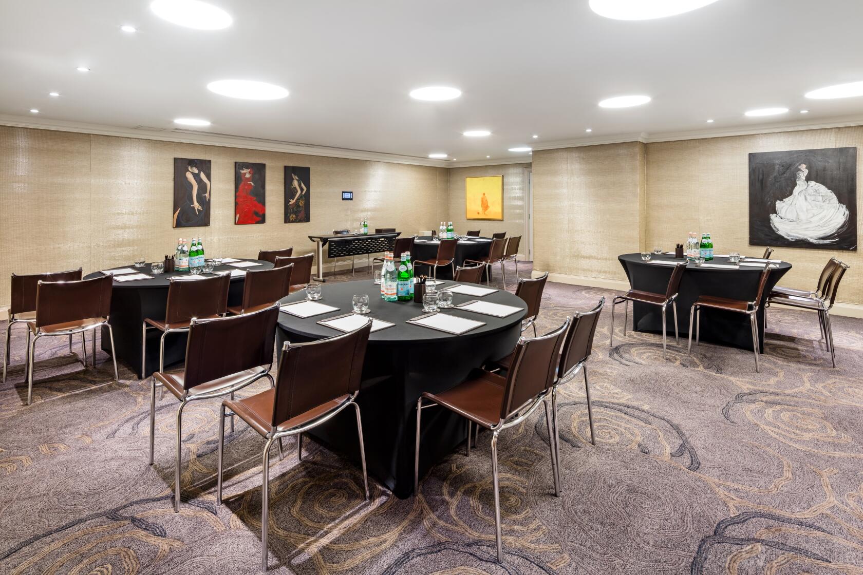 A meeting room with round tables, brown chairs, bottled water, and modern artwork at Radisson Blu Hotel, London Euston Square.