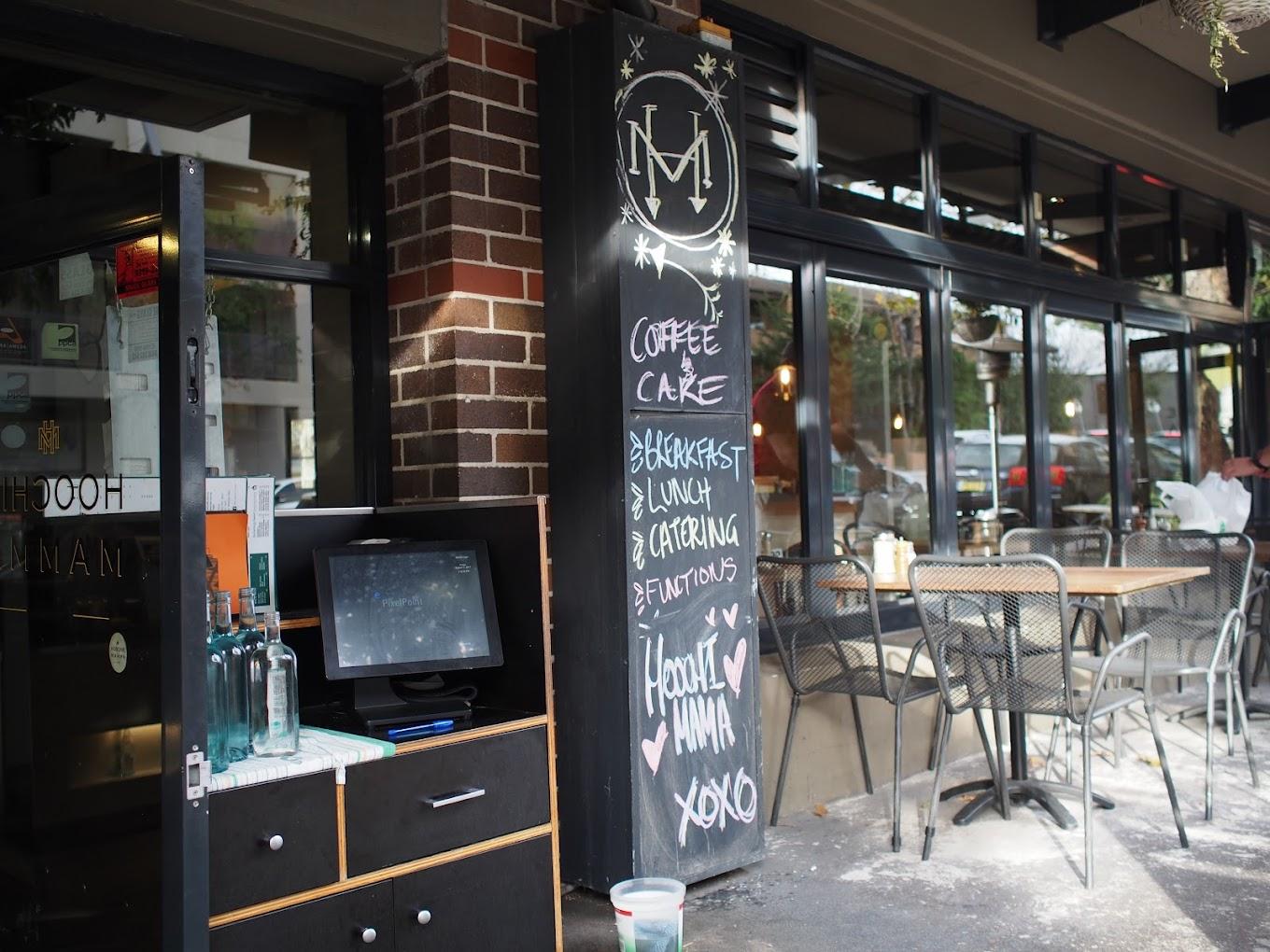 A café with outdoor sidewalk seating, large windows, and a chalkboard menu at Hoochie Mamma.