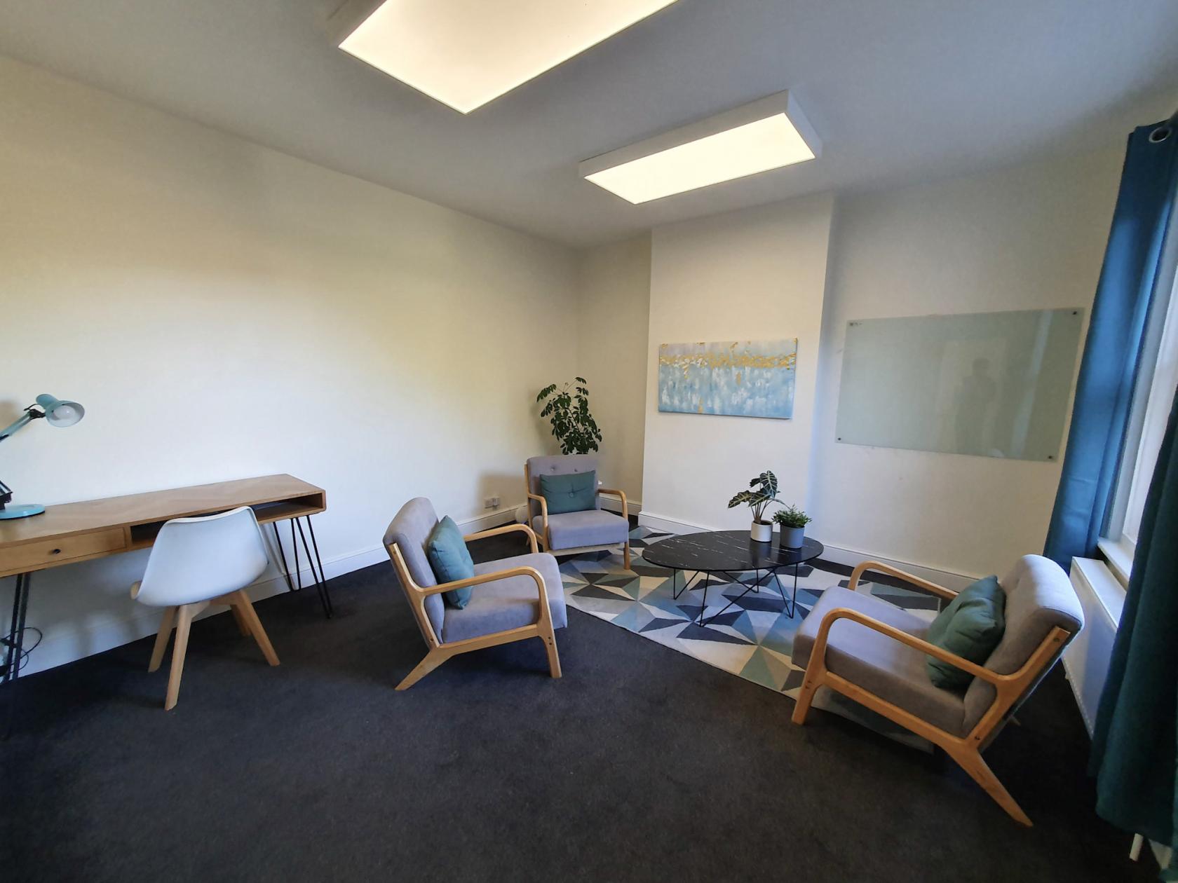 A meeting room with armchairs around a round table, a desk, and wall art at Oxford CBT.