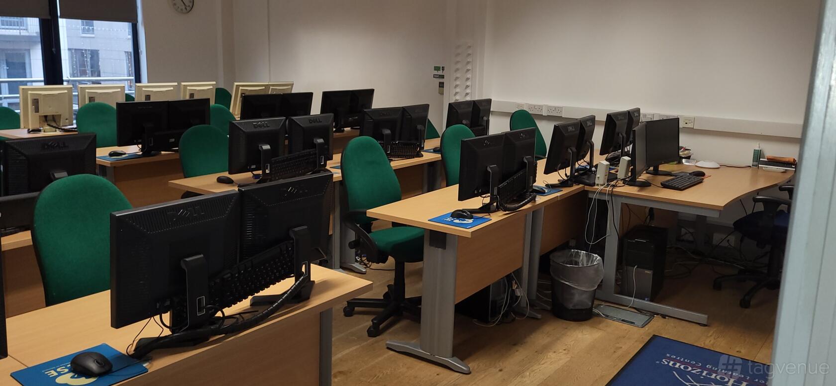 A training room with rows of desks, desktop computers, and green chairs at Nexus Human Training Centre.