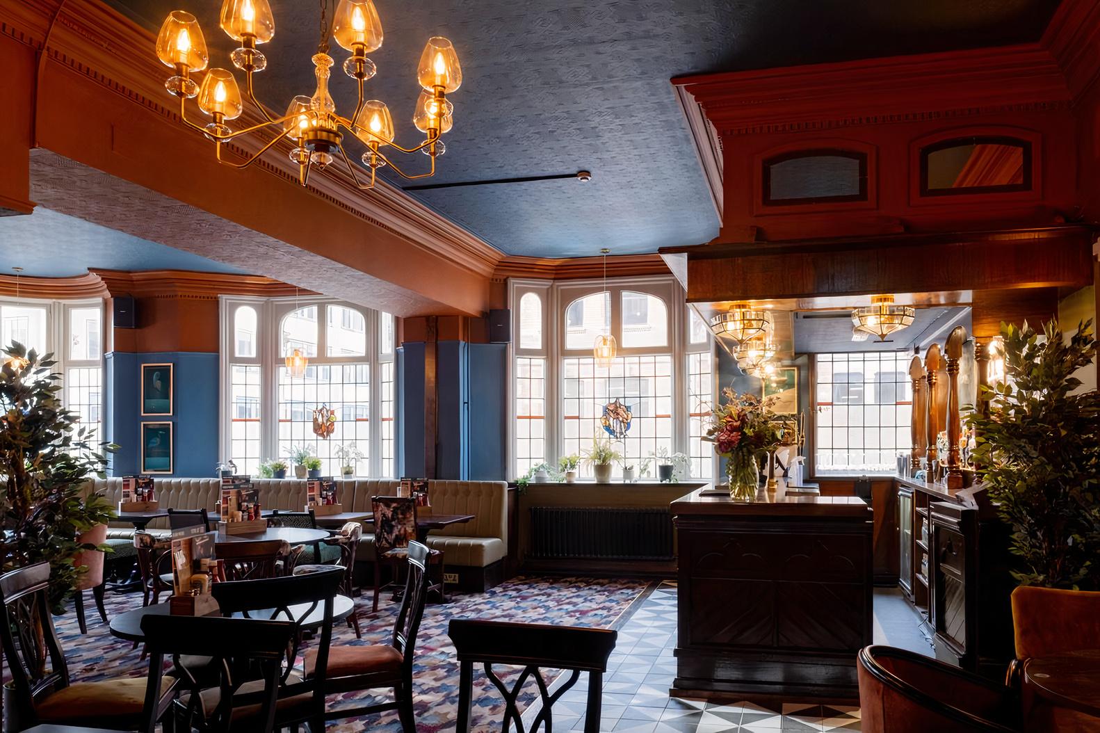 An event space in a pub with stained glass windows, upholstered chairs, chandeliers, and patterned flooring at The Royal.