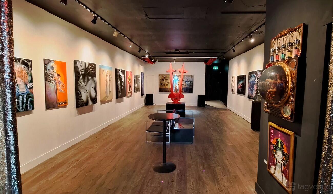 A gallery with colorful modern art on white walls, wooden floors, and a sculptural centerpiece at Super Wonder Gallery.
