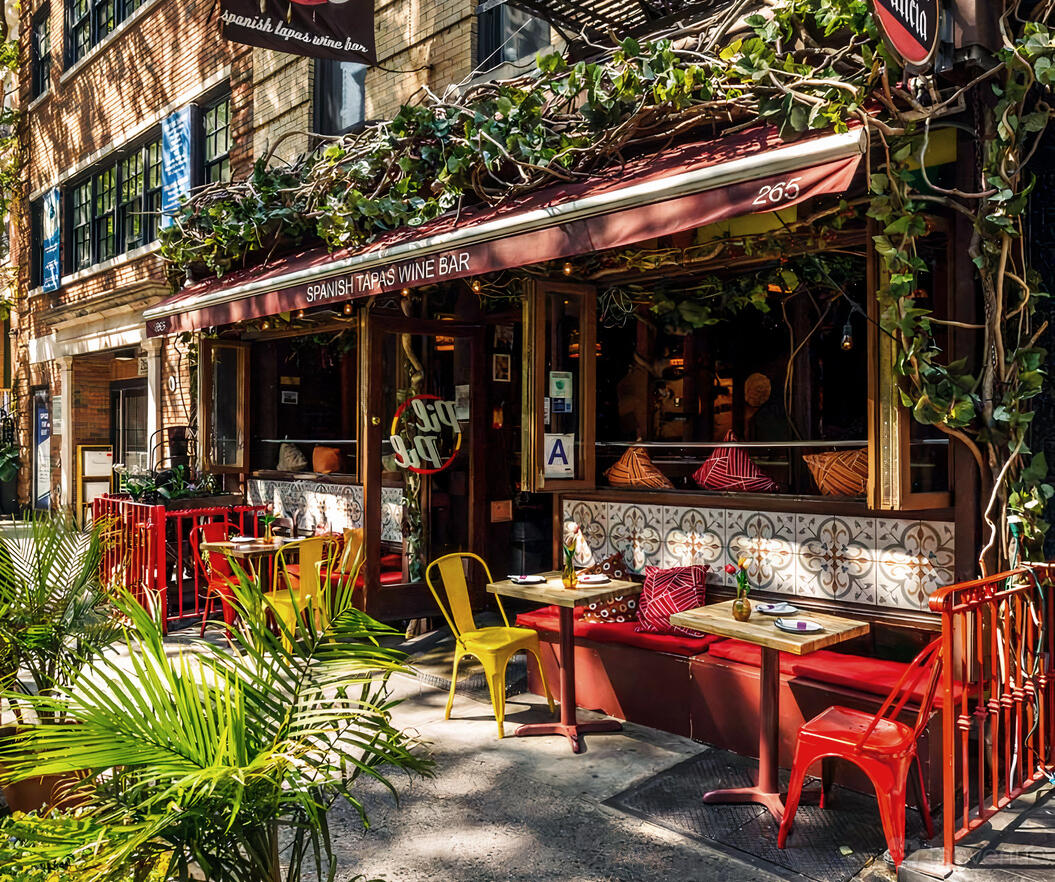 An outdoor dining area with red fencing, yellow chairs, and leafy vines at Pil Pil restaurant.