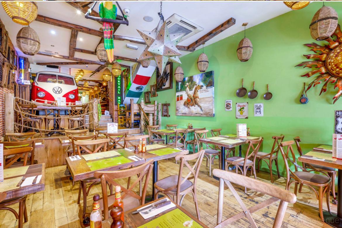 A restaurant with wooden tables, eclectic decor, green walls, and ceiling lanterns at GrillShack Steakhouse and Cocktail bar.