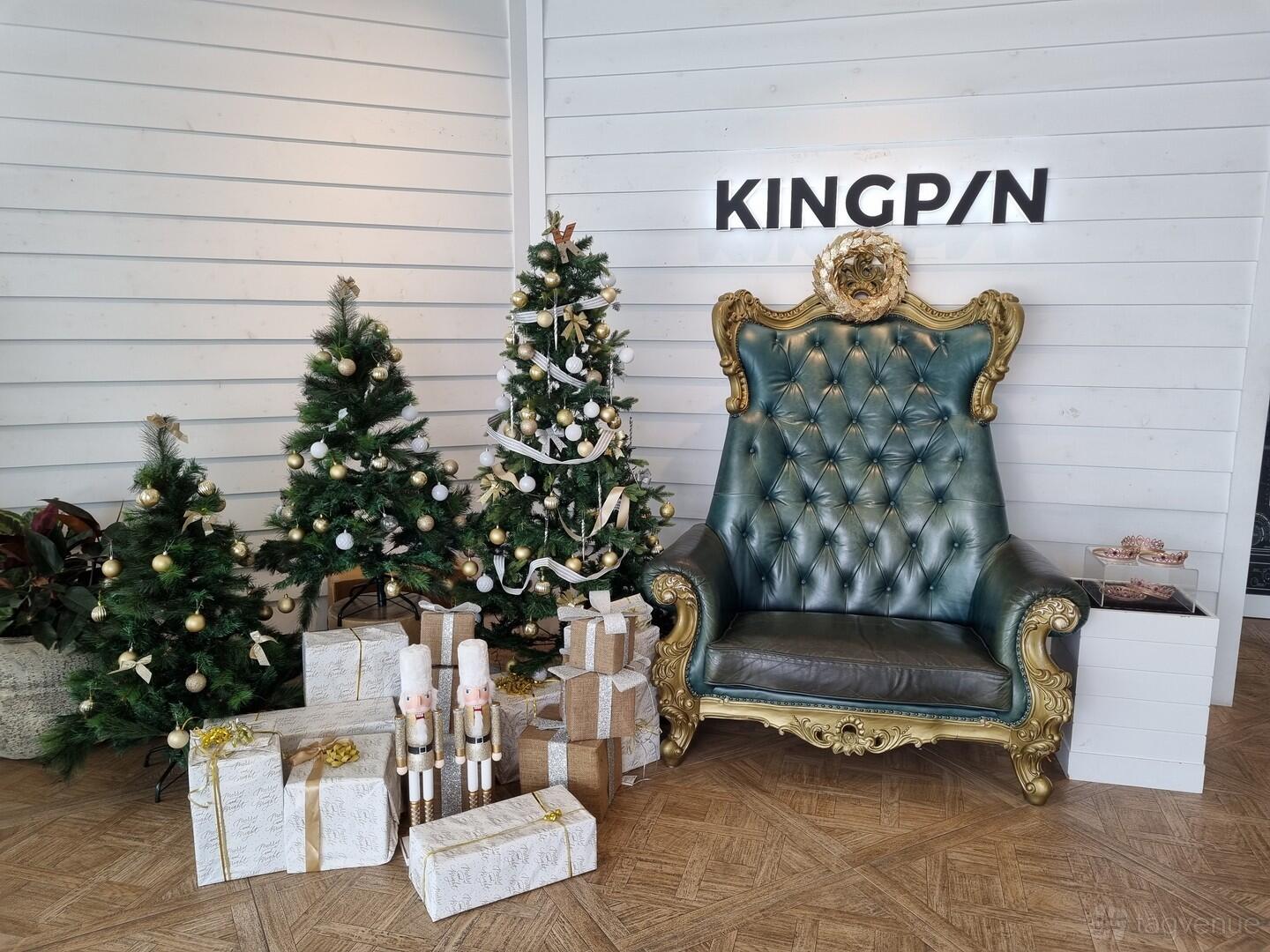 A seating area with a gold-trimmed green armchair, Christmas trees, and wrapped presents at Kingpin Chermside.