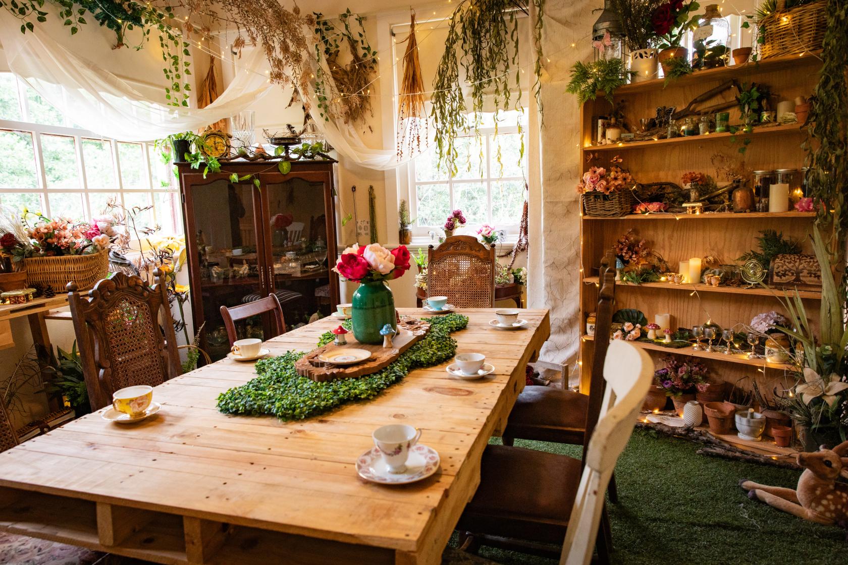 A house event space with a rustic wooden dining table, teacups, floral arrangements, and lush plants at Curious Events Co.