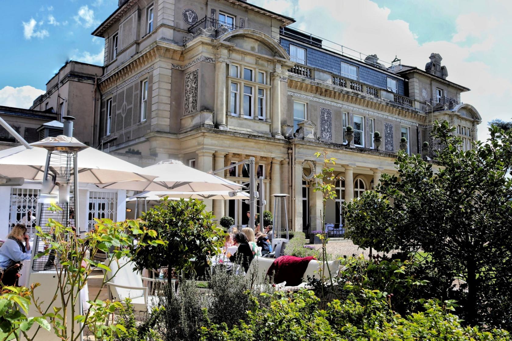 A hotel with ornate stone facade, large windows, and outdoor seating beneath umbrellas at Down Hall Hotel.
