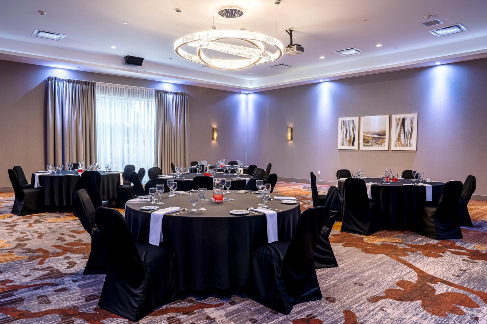 A hotel ballroom with black round tables, banquet chairs, a large chandelier, and carpeted floors at DoubleTree by Hilton Kitchener.