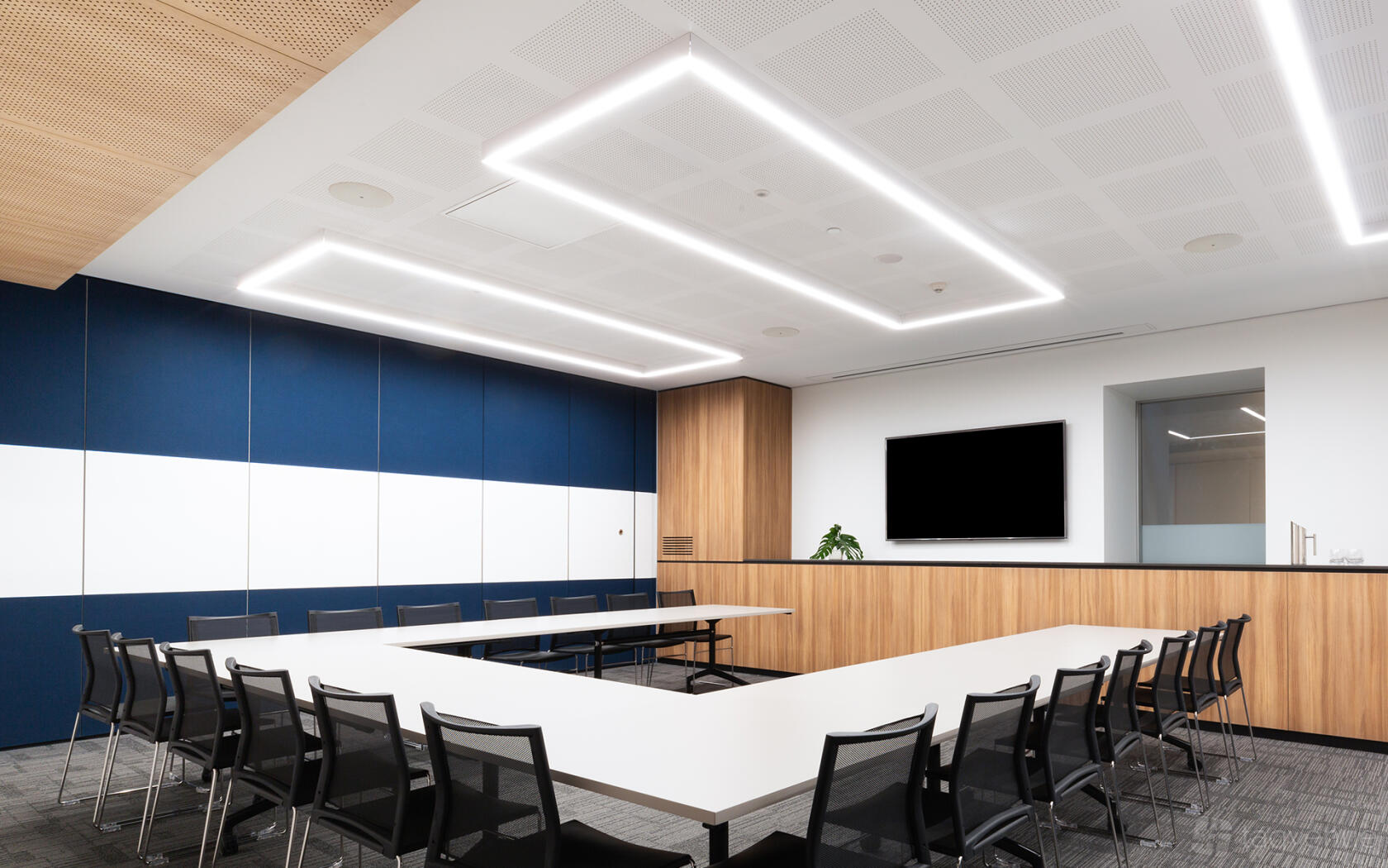 A meeting room with U-shaped black mesh chairs, wood accent walls, and a large screen at Flex by ISPT at George Place.