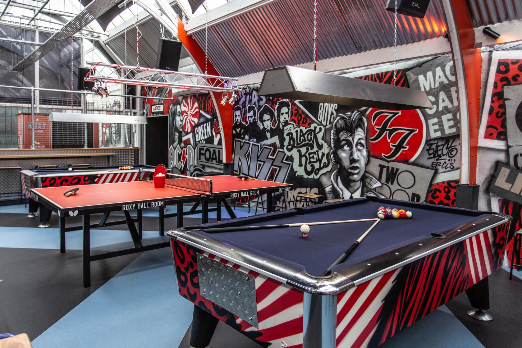 A bar with graffiti-covered walls, skylights, and game tables including pool and table tennis at Roxy Ball Room Leeds Merrion Street.
