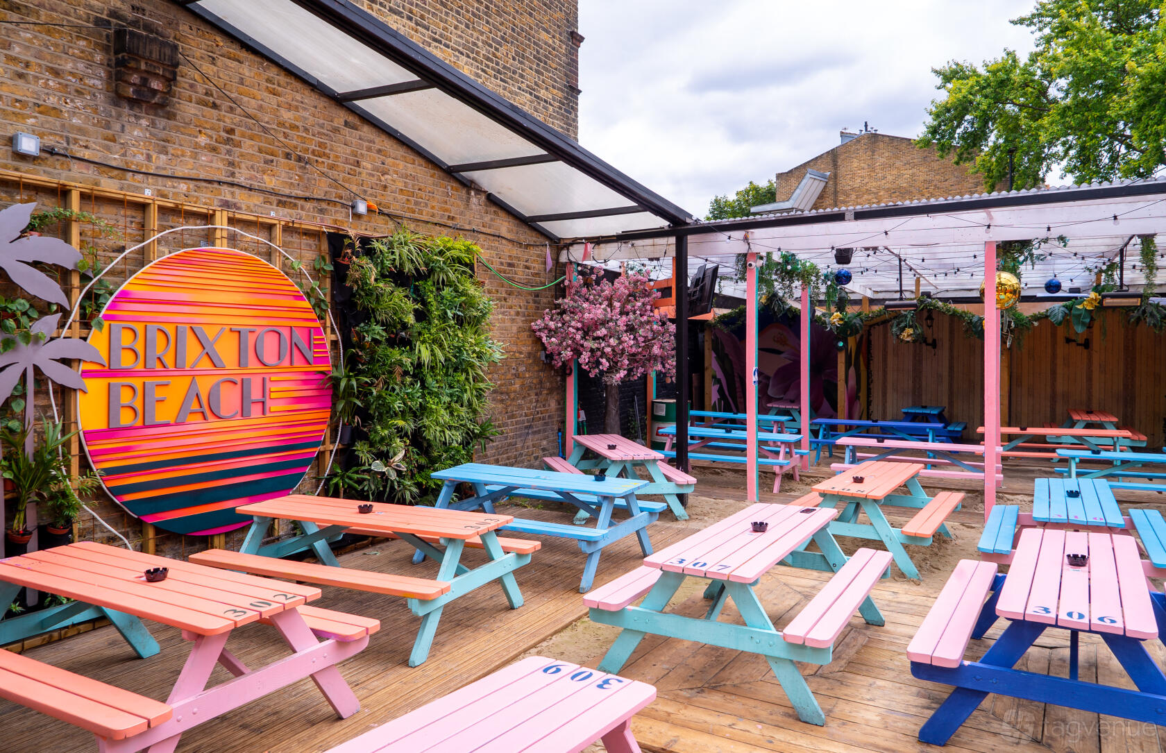 An outdoor nightclub area with colorful picnic tables, wooden decking, and a Brixton Beach sign at Brixton Jamm.
