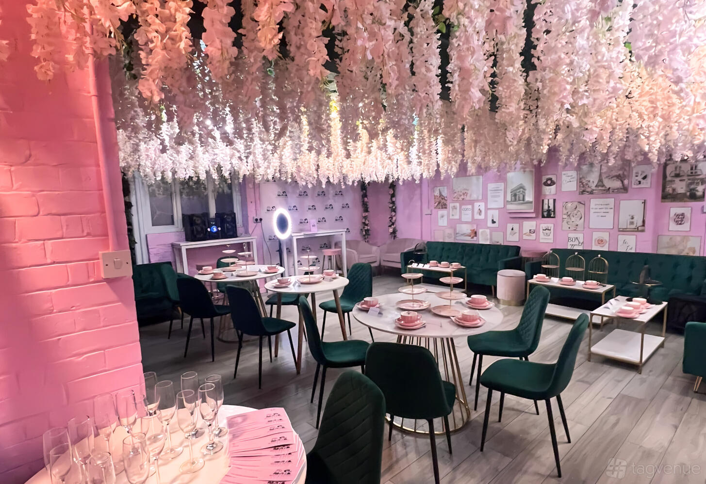 A cafe with cascading floral ceiling decor, pink brick walls, green velvet chairs, and round tables at Beauty and The Feast.
