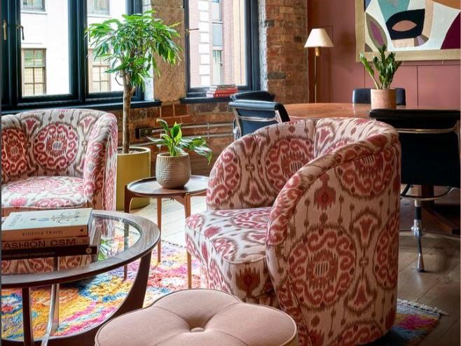 A meeting room with patterned armchairs, potted plants, and large windows with brick detailing at 1 Warwick.