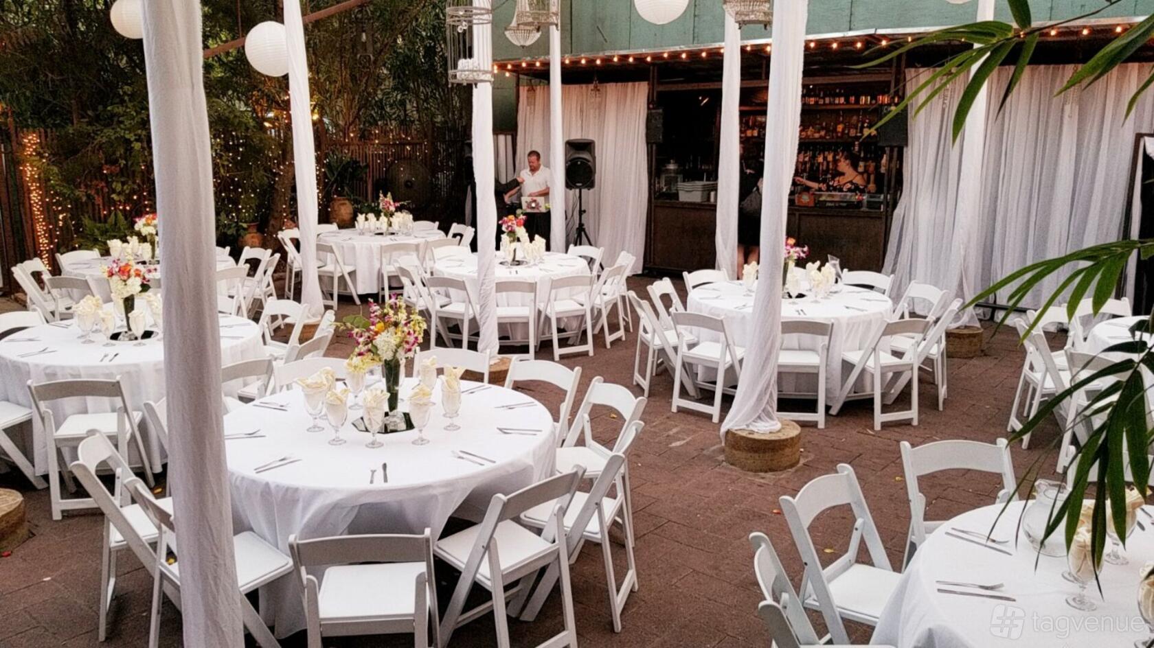 An outdoor terrace with round tables covered in white linens, floral centerpieces, and string lights at AvantGarden.