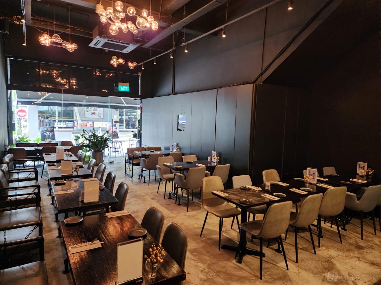 A dining room with sleek dark tables, upholstered chairs, and large windows at Perle Noire Oyster & Grill Bar.