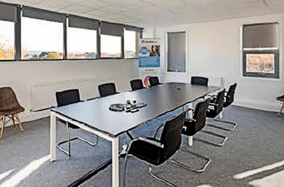 A meeting room with a long rectangular table, eight black chairs, and large windows at Biz Hub Middlesbrough.