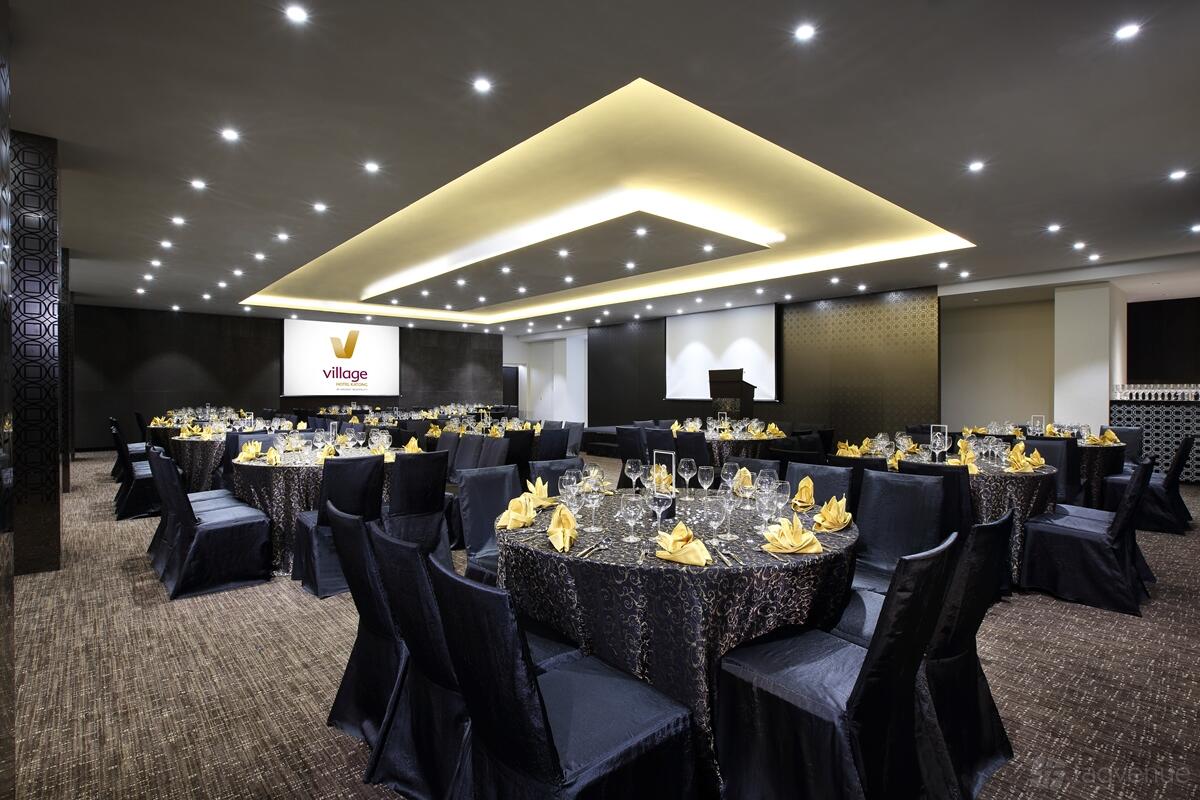 An event space with round tables draped in dark linens and yellow napkins under recessed ceiling lights at Village Hotel Katong.