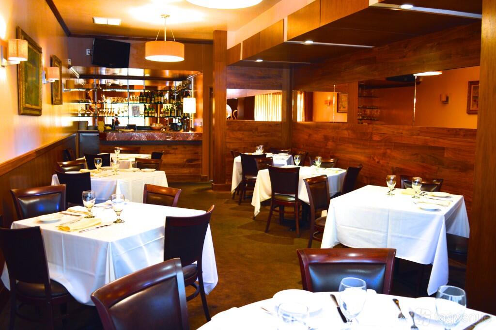 A restaurant dining room with white linen tables, dark wood chairs, and ambient lighting at Marino Restaurant.