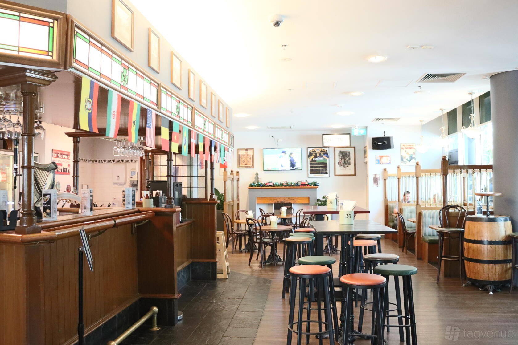 A hotel pub with a wooden bar, high tables and stools, Irish flags, and framed photos at Novotel Perth Langley.
