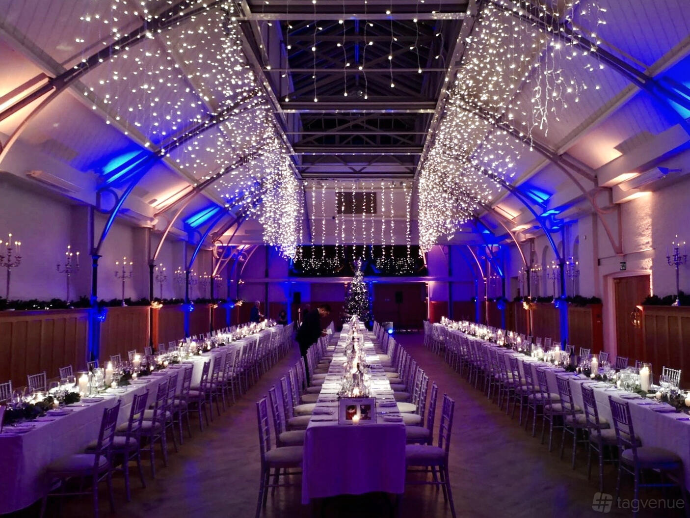 An event venue with vaulted ceilings, hanging fairy lights, and long banquet tables set for dining at The HAC.