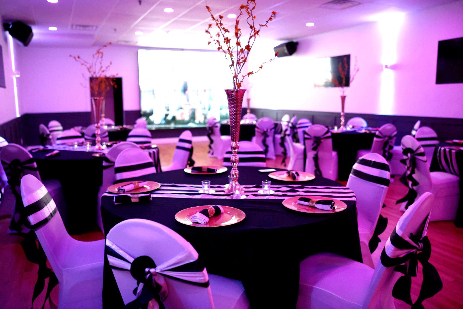 A hall with round tables covered in black and white linens, gold chargers, and chair sashes at The Space Next Door.