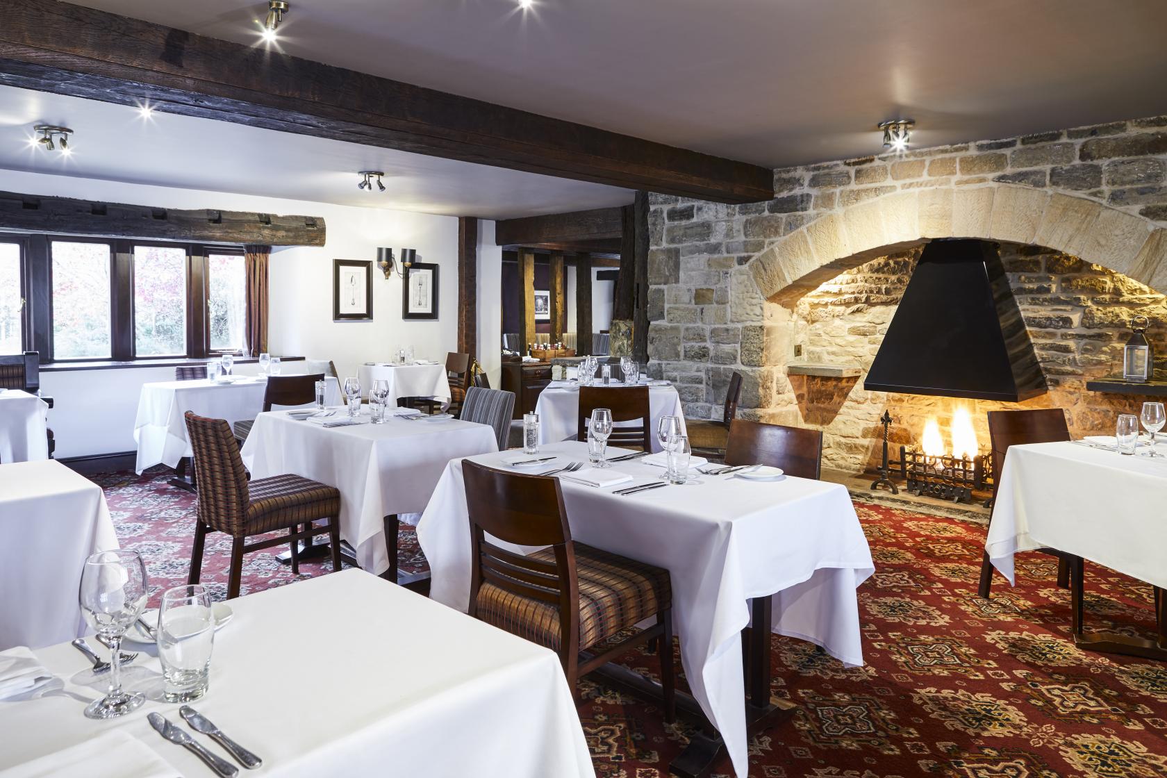 A restaurant with exposed beams, stone fireplace, and tables with white linens at Mercure Tankersley Manor Hotel and Spa.