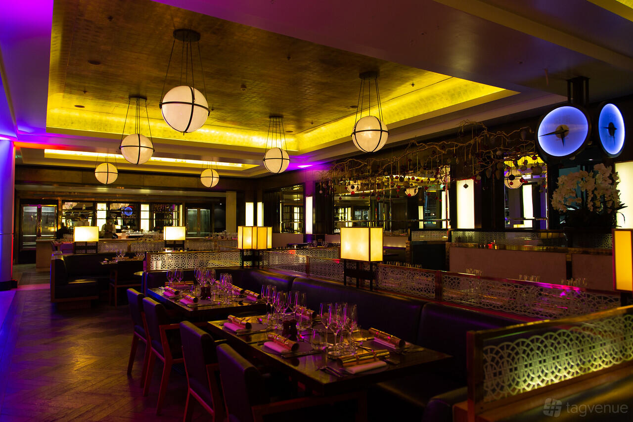 A restaurant with globe pendant lighting, dark wood tables set for dining, and illuminated ceiling panels at St Pancras by Searcys.
