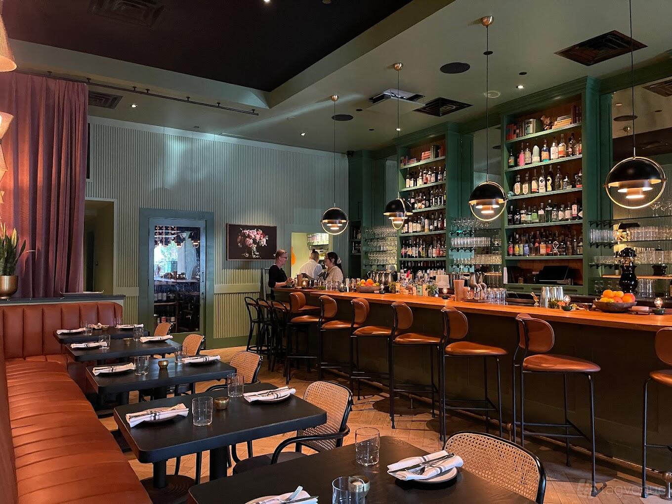 A restaurant with a long wood bar, leather banquette seating, and globe pendant lights at Zola + BarZola.